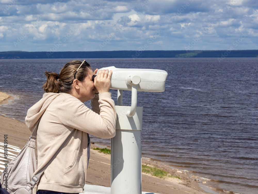 On June 19, 2022 in Cheboksary, a woman looks through a binocular telescope at tourists on the embankment