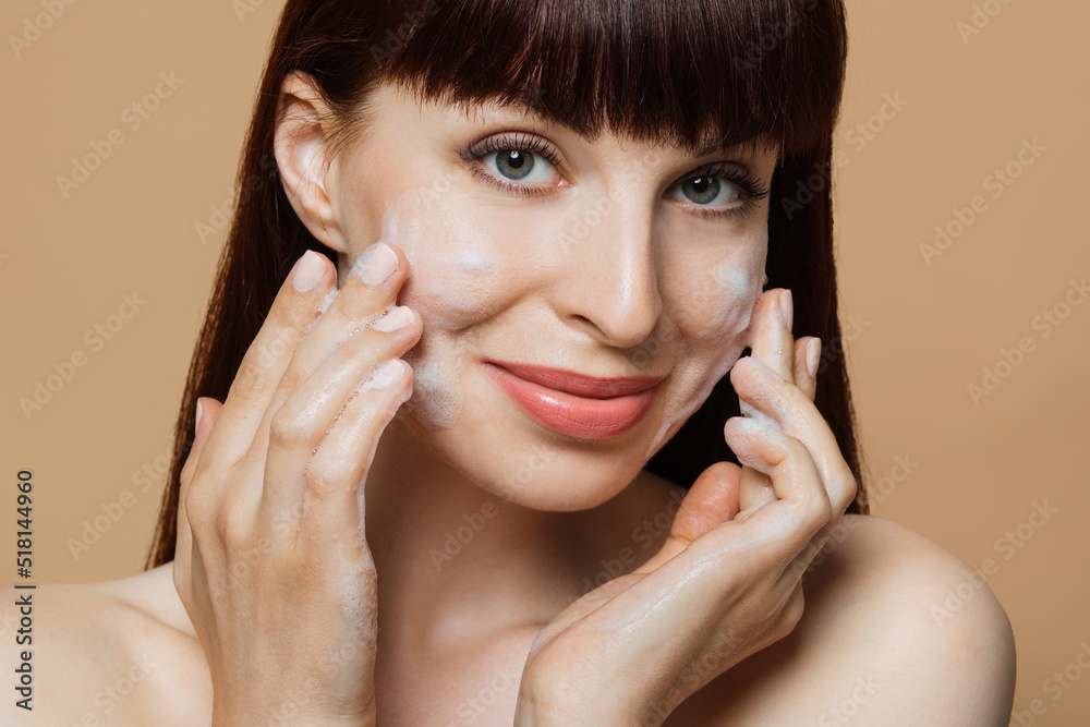 Happy smiling young woman cleaning face with soap foam studio portrait. Pretty girl massaging skin on cheeks. Face skincare natural cosmetic. Morning routine, facial beauty treatment. White copy space Happy smiling young woman cleaning face with soap foam studio portrait. Pretty girl massaging skin on cheeks. Face skincare natural cosmetic. Morning routine, facial beauty treatment. White copy space