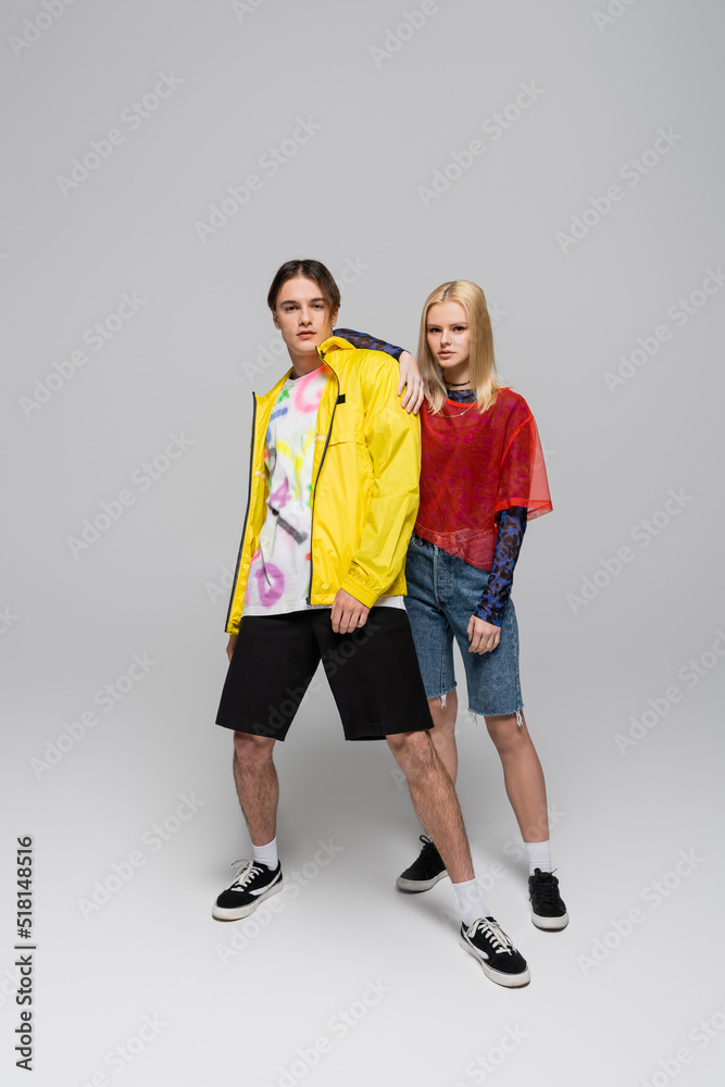 Full length of trendy couple looking at camera on grey background. Full length of trendy couple looking at camera on grey background.