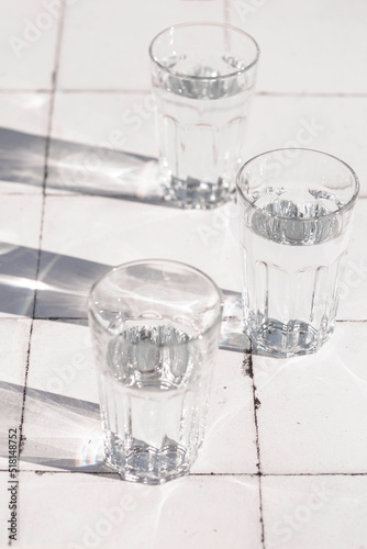 glass and sharp shadows stands on a white tiled table. top view of glass
