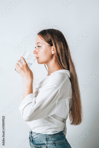 Asian girl with purple drinks water from a plastic bottle on a white isolated background. Generation Z. The concept of thirst