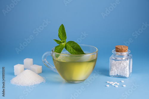 A cup of green tea with mint leaves on one side is sugar on the other stevia tablets on a blue background. The choice of a sweetener in tablets or regular sugar. An alternative to sugar for diabetics. photo