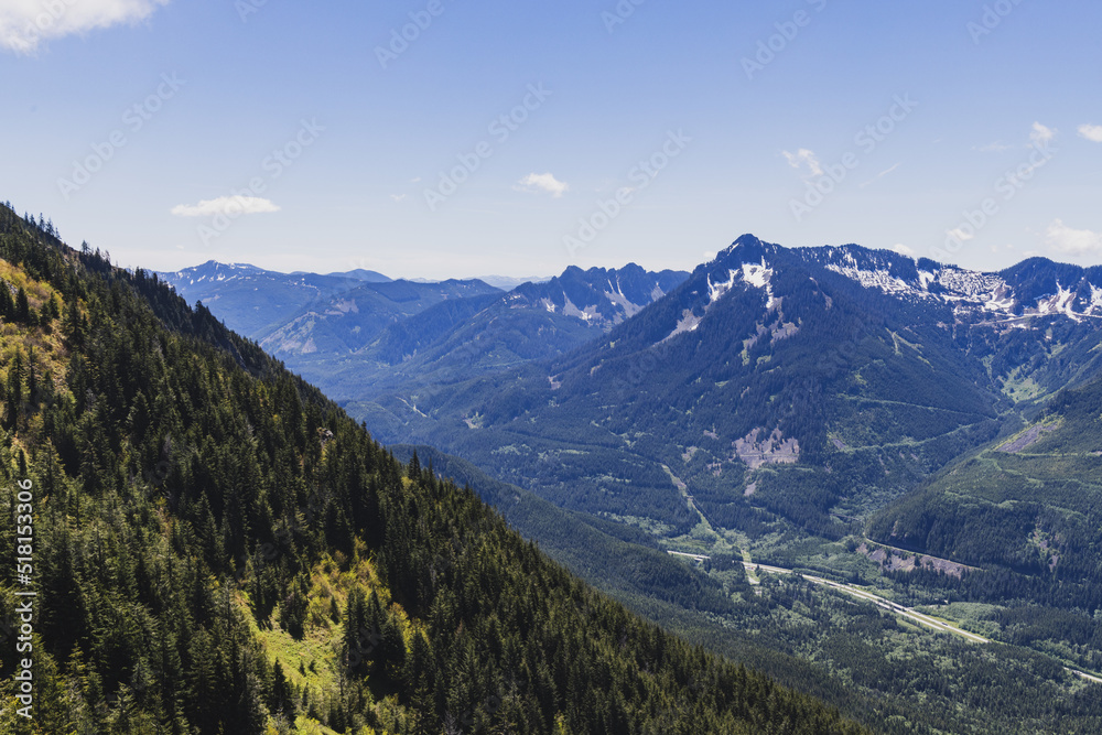 A tree-lined hillside with a more mountains in the background and a hiking trail
