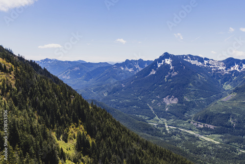 A tree-lined hillside with a more mountains in the background and a hiking trail