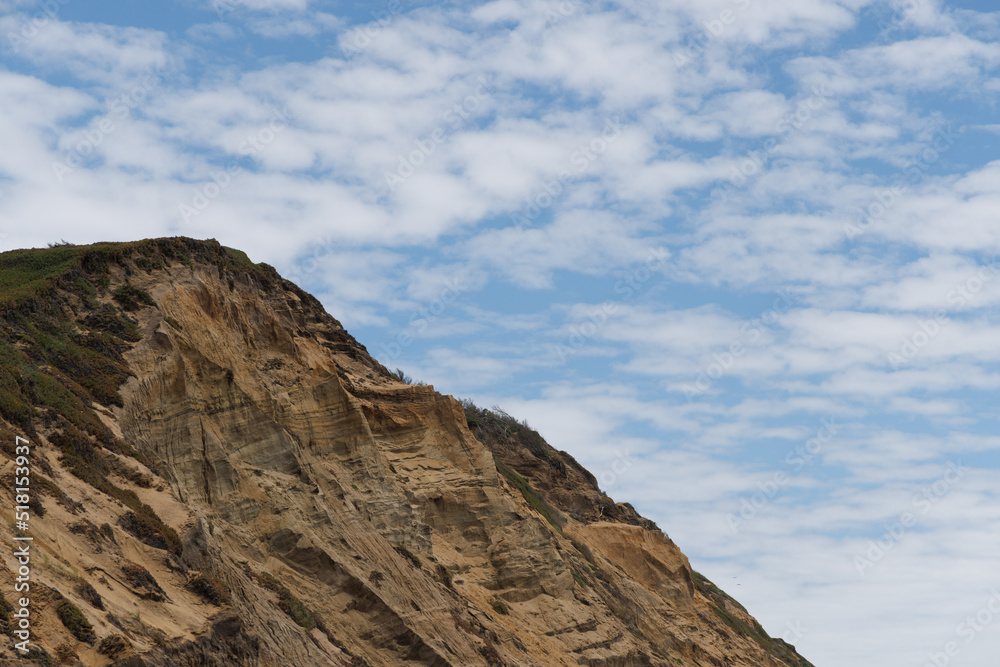 A rocky hill on the California coast with blue cloudy skies above