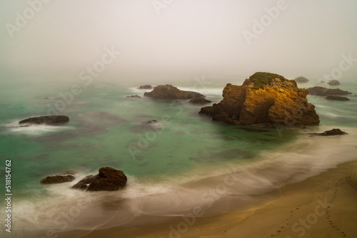 Long exposure of the rocky California coastline making dreamy waves around haystacks on a foggy morning