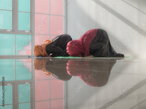 Two Muslim women making prostration praying in Sujud pose. The shiny floor reflected the reflection of two Muslim lady praying. photo