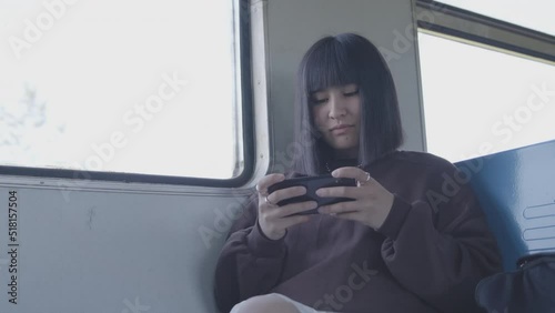 A young woman sits in a train at the window, plays games on a smartphone, smiles. Outside the forest. Slow motion 4k footage.