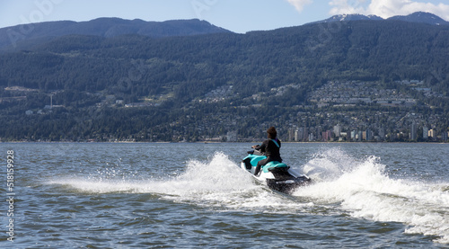 Adventurous Caucasian Woman on Water Scooter riding in the Ocean. Modern City and mountains in background. Downtown Vancouver, British Columbia, Canada.