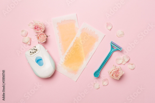 Wax strips, modern epilator and razor with flowers on color background, top view