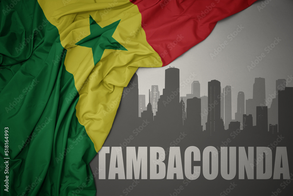 abstract silhouette of the city with text Tambacounda near waving colorful national flag of senegal on a gray background.