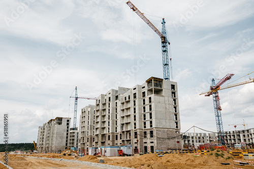 unfinished apartment buildings at the construction site and cranes in background
