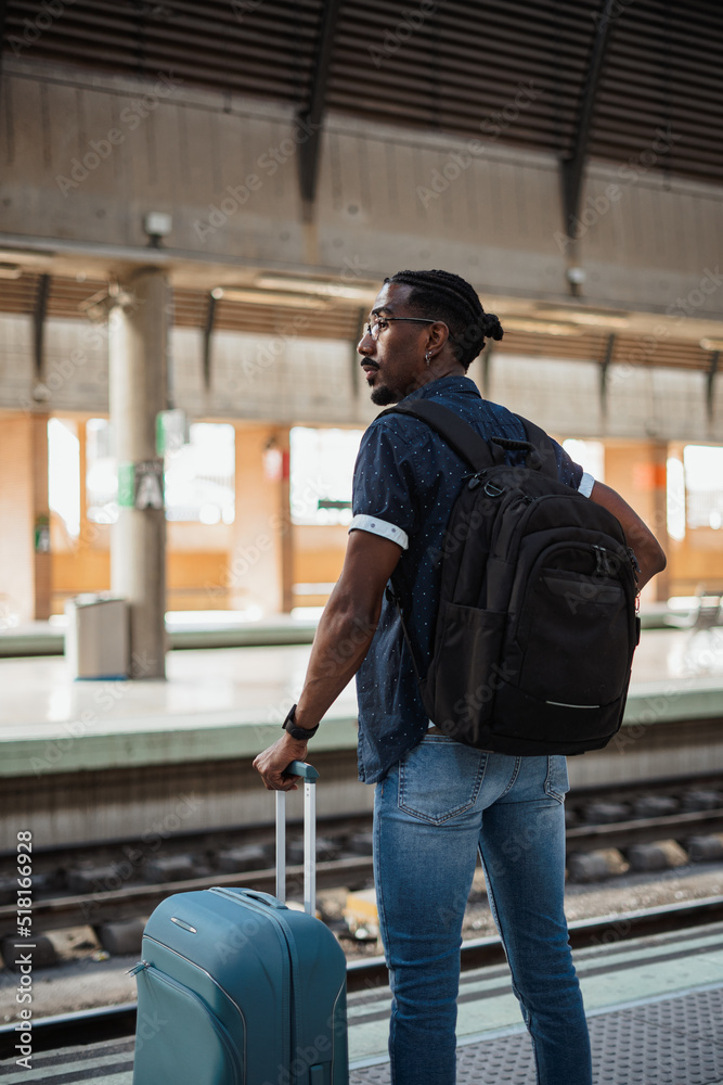African male standing next to a platform at a train station while he waits for the train African male standing next to a platform at a train station while he waits for the train