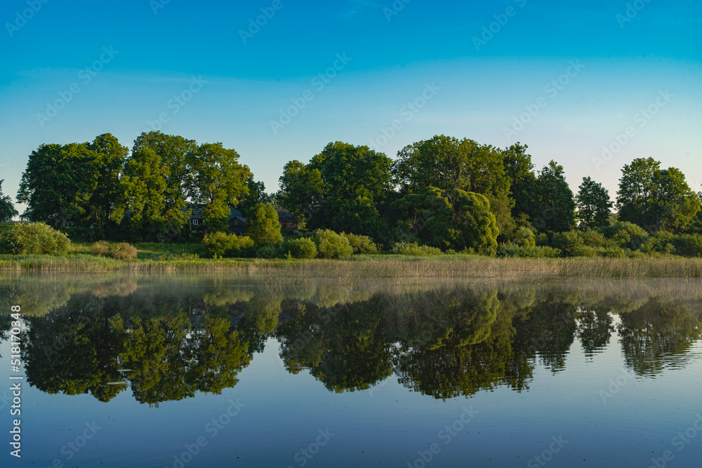 Landscape view on the river and coast with trees in morning light and reflection in water