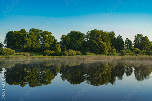 Landscape view on the river and coast with trees in morning light and reflection in water