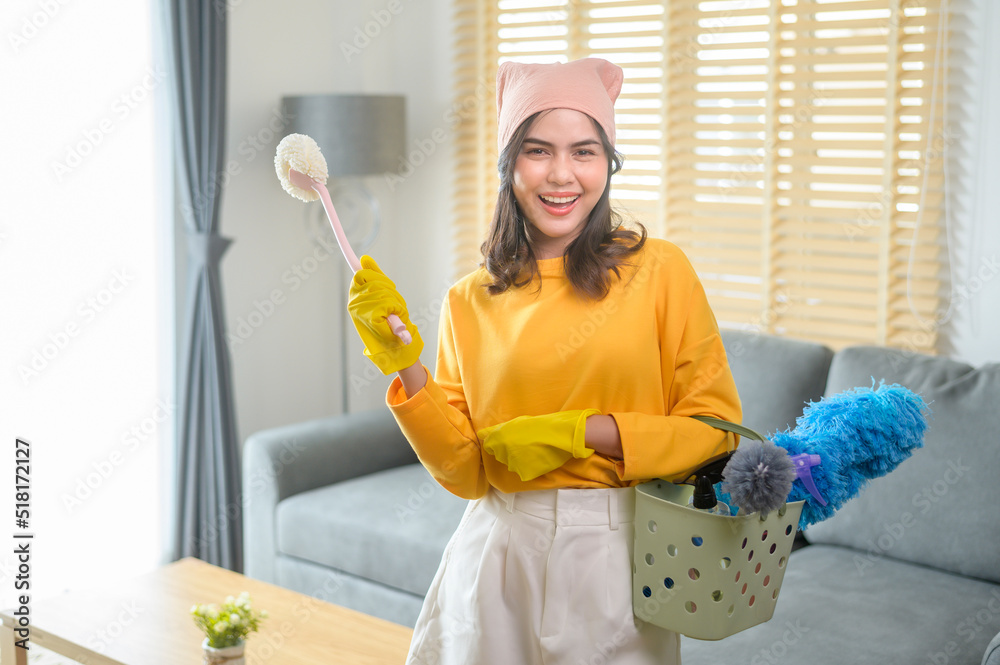 Young happy woman wearing yellow gloves and holding a basket of cleaning supplies in living room. Young happy woman wearing yellow gloves and holding a basket of cleaning supplies in living room.