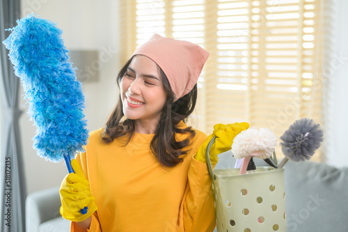 Young happy woman wearing yellow gloves  and holding a basket of cleaning supplies in living room. photo