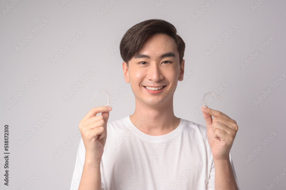 Young smiling man holding invisalign braces over white background studio, dental healthcare and Orthodontic concept.. Young smiling man holding invisalign braces over white background studio, dental healthcare and Orthodontic concept..