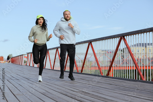 A woman and a man in sweatshirts run on the bridge in the morning workout