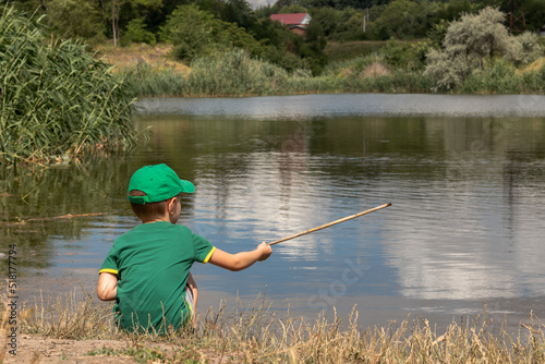  a boy in a green T-shirt and cap sits on the background of the water surface. back view image