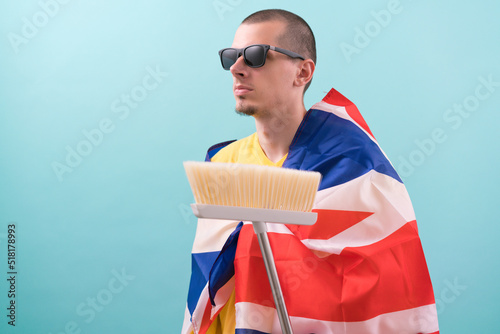 Man in sunglassed with a broom covered in British flag on a blue background. Work. Young. Handle. Housing. Handsome. Equality. Dust. Job. Passion. Posing. Positive. Real Estate. Worker. Dirty photo