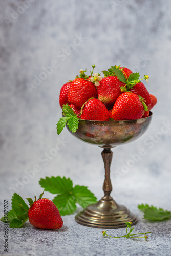 Ripe strawberries in an old silver vase on a gray background.