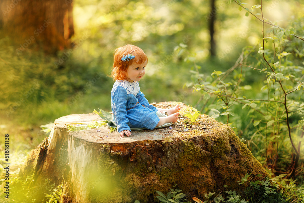 Baby red hair girl in blue dress sitting on a big tree stump in the ...