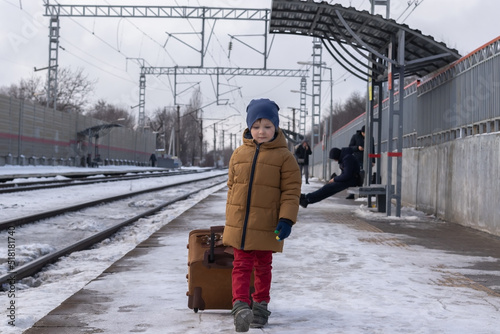 Wallpaper Mural a boy dressed in a coat and a winter hat walks along the railway platform with a suitcase. winter railway station concept Torontodigital.ca