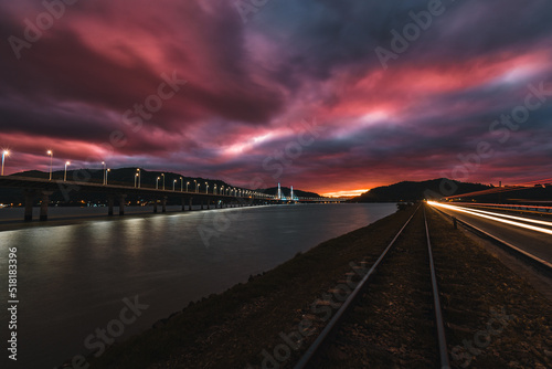 Landscape with clouds and lights from moving cars. Bridge lit in the background.