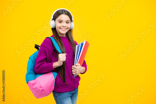 Back to school. Teenager school girl with backpack and headphones hold books ready to learn. School children on isolated yellow studio background.