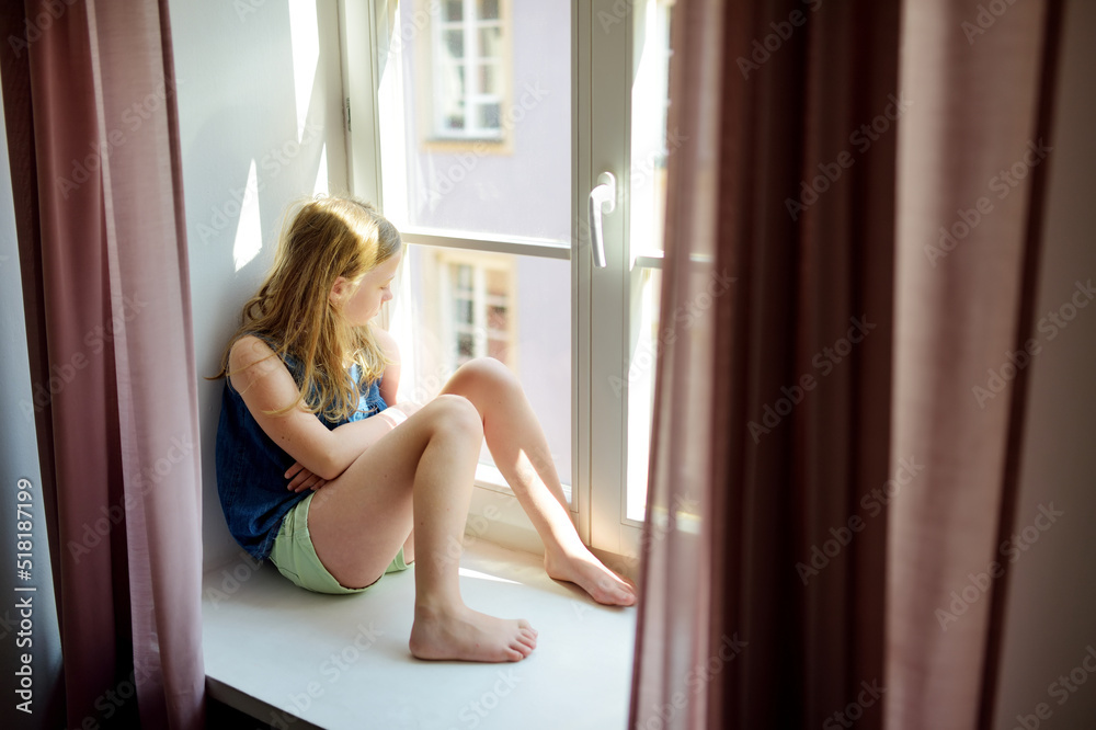 Beautiful preteen girl looking out the window. Young girl sitting on a windowsill. Beautiful preteen girl looking out the window. Young girl sitting on a windowsill.