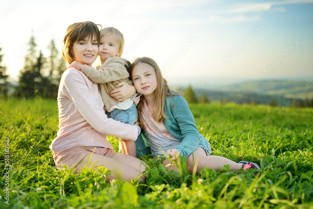 Two sisters and their toddler brother having fun outdoors on sunny summer day. Children exploring nature. High mountains and green hills in summer or spring. Two sisters and their toddler brother having fun outdoors on sunny summer day. Children exploring nature. High mountains and green hills in summer or spring.