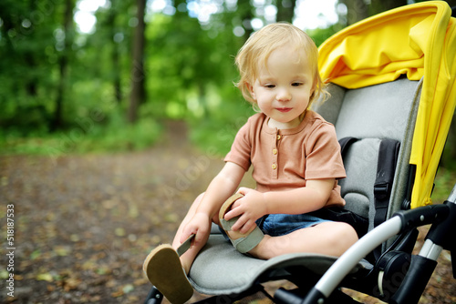 Sweet toddler boy sitting in a stroller outdoors. Little child in pram. Infant kid in pushchair. Summer walks with kids.