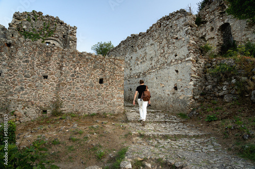 Tourist man with backpack exploring ruins of old city of Mystras, UNESCO world heritage archeological sight. photo