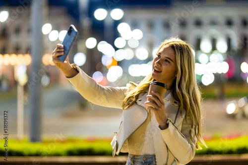 Young woman taking selfie with a smartphone while walking on the city streets on the coast during the night