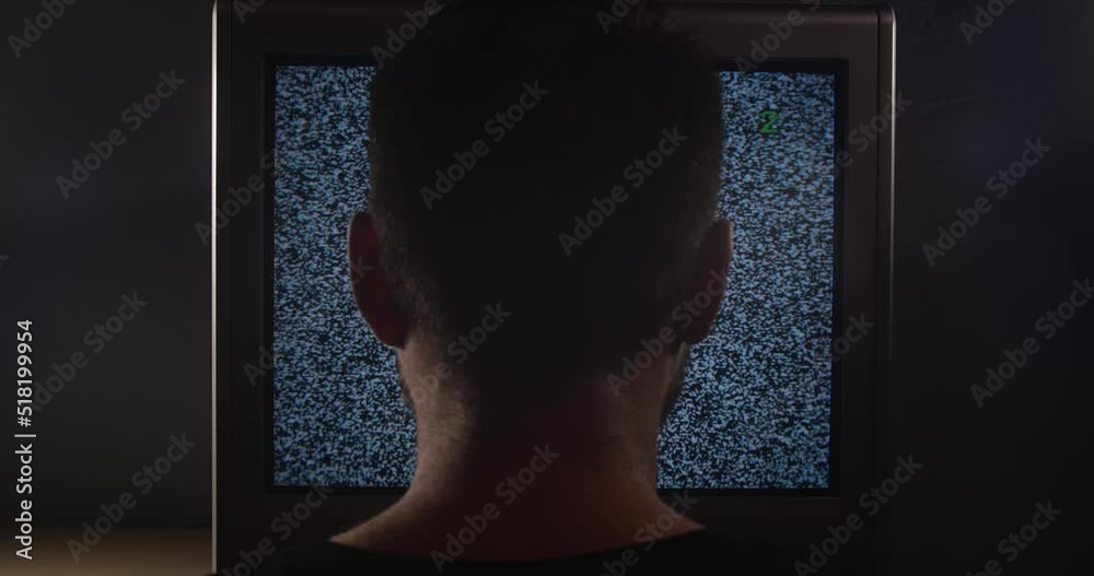 Man sitting near old analog TV screen with white noise. Close up back of male head turning on, turning off, changing channels. Concept of zombification, utility bills. Man sitting near old analog TV screen with white noise. Close up back of male head turning on, turning off, changing channels. Concept of zombification, utility bills.