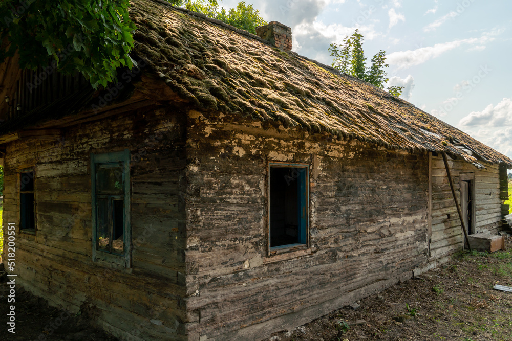 An old wooden uninhabited house. A small house in the village with a sunken roof and walls overgrown with moss. Destroyed housing after the cataclysm and poverty in Russia.