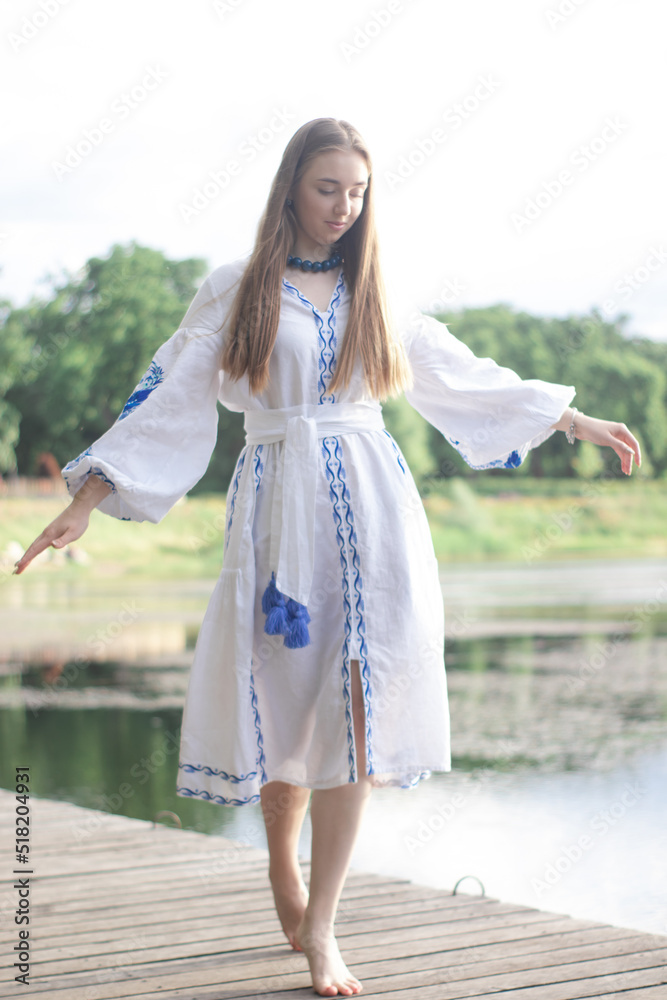 a girl in an embroidered Ukrainian shirt sits on the pier, the reflection of clouds in the water of the lake. On the shore of the sky. vyshyvanka day. freedom. patriot
