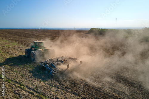 Aerial view of tractor plowing agriculural farm field preparing soil for seeding in summer