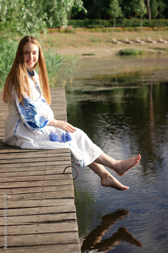 Girl in embroidered national Ukrainian costume on a pier on the shore of the lake. Independence day of ukraine, constitution, vyshyvanka day. young woman in blue dress outdoors