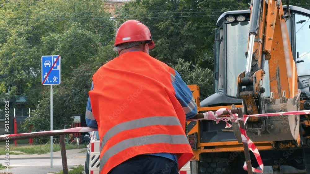 Road works. The excavator digs a trench. A road worker in an orange vest observes and corrects the work of an excavator. Road works. The excavator digs a trench. A road worker in an orange vest observes and corrects the work of an excavator.