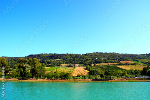 Perfect view from Santarelli lakes in Piane di Moresco with the calm aquamarine waters of the lake reaching to the thriving Marche hilly landscape with greenery and a white house in the middle