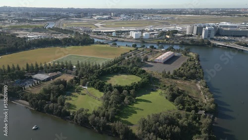 Aerial zoom in flying over the cooks river, park with green trees, playground and indoor and outdoor sport stadium with Sydney Airport in the background. photo