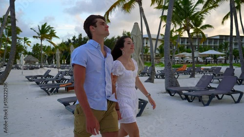 Boyfriend girlfriend dating couple takes walk on white sandy beach. Private luxurious hotel resort property. photo