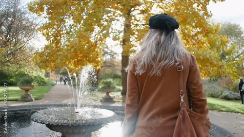 blonde English lady with dark blue hat standing by a fountain in the botanical garden in Oxford Uk, then turning around and smiling into the camera photo