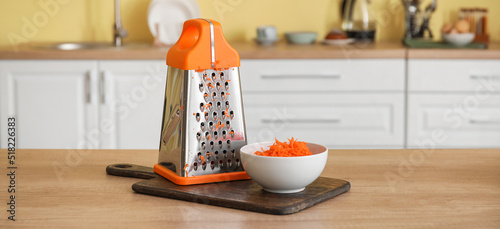 Bowl with fresh carrots and grater on kitchen table