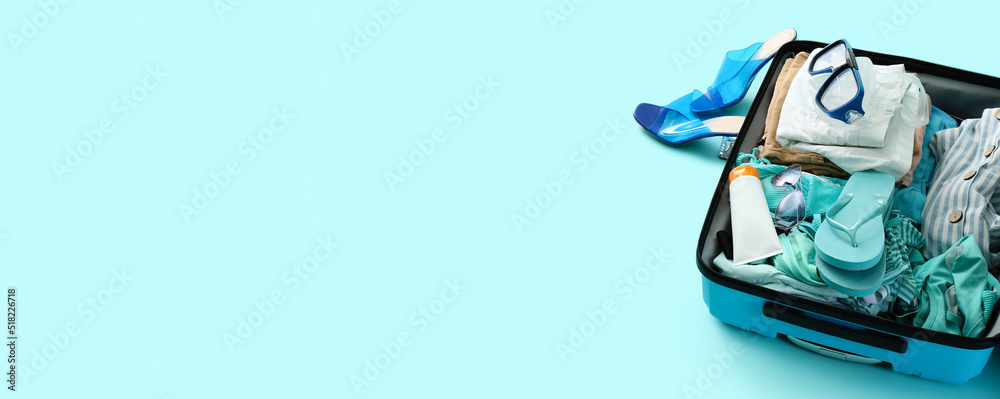Open suitcase with clothes and beach accessories on light blue background with space for text