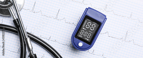 Pulse oximeter and stethoscope on cardiogram, top view photo