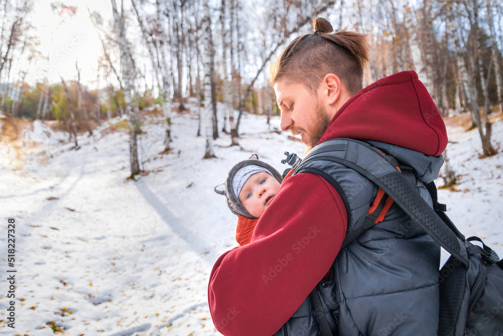The baby walks through the winter forest in the arms of his babywearing father.