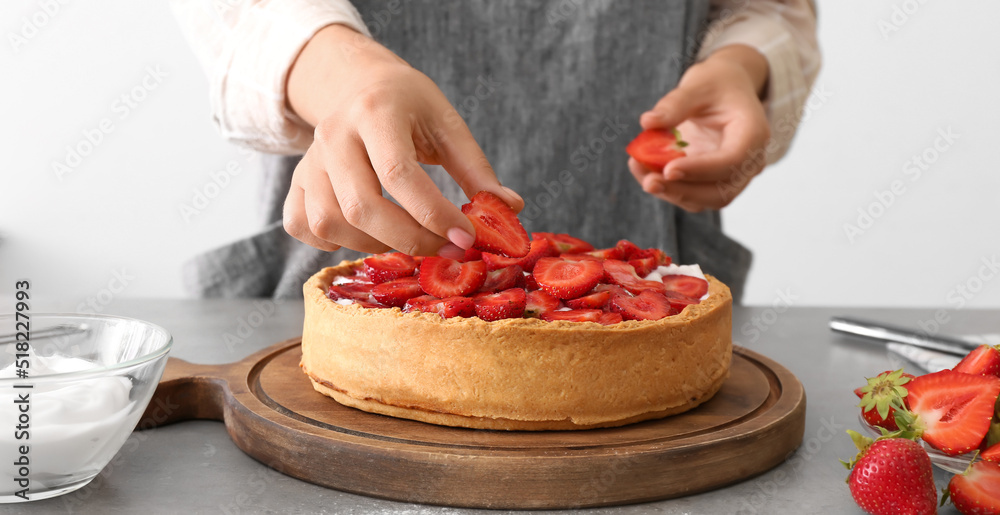 Woman decorating tasty pie with strawberry in kitchen, closeup
